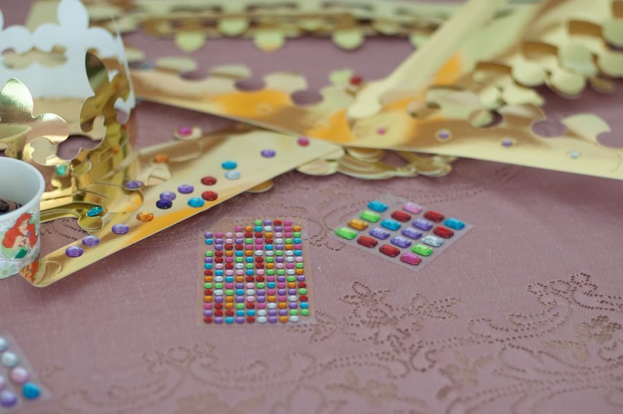 Children decorating gold crowns with gems at a princess party craft table
